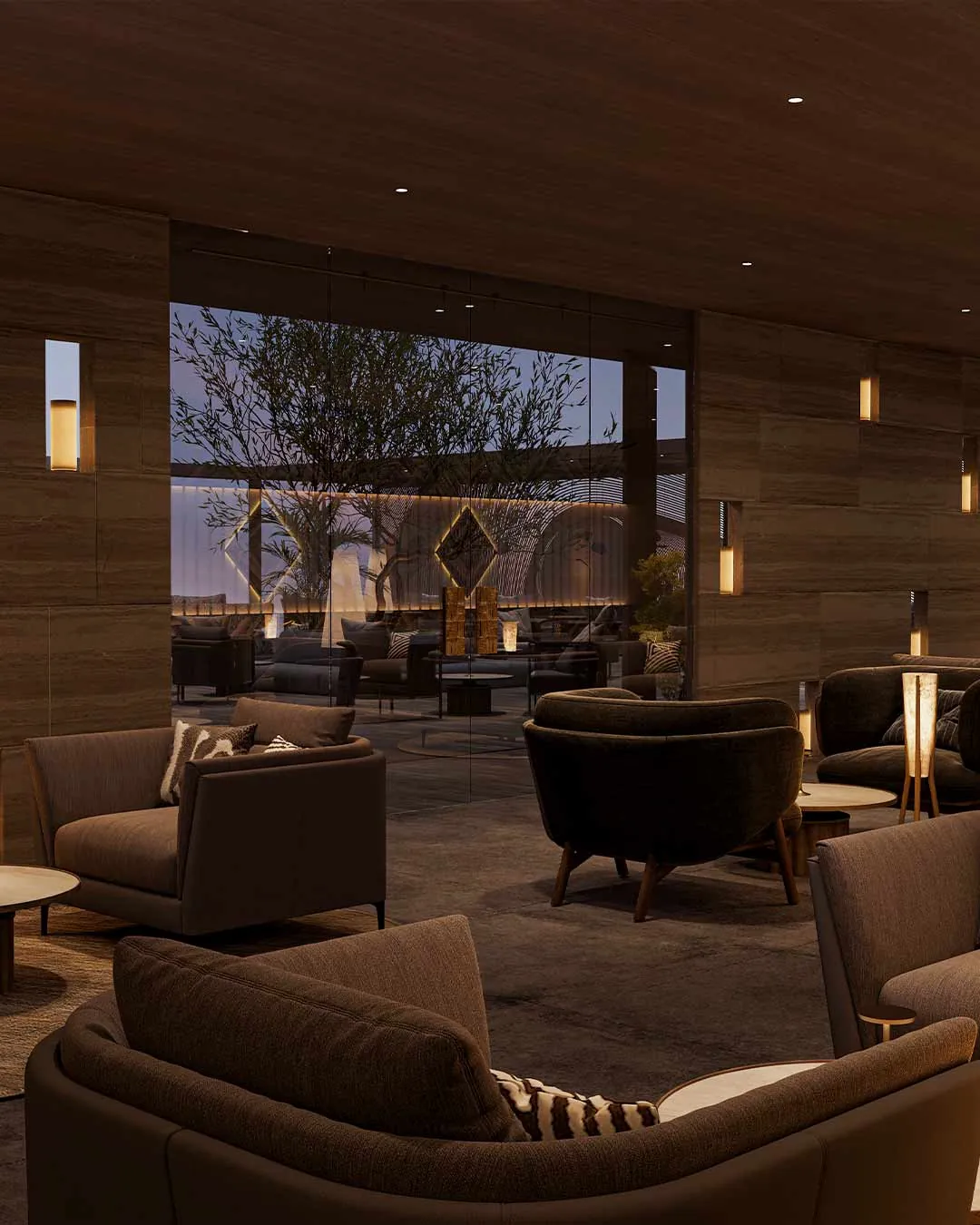 Lounge with deep sofas and warm evening lighting, with trees visible through tall windows